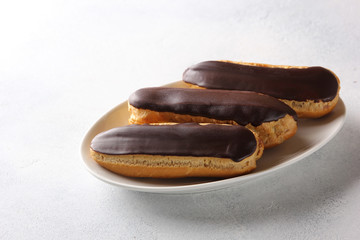 Dessert. Eclairs with chocolate glaze. Cake with cream on the white plate on a light background. Background image, copy space
