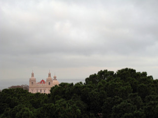 Fototapeta na wymiar Iglesia entre arboles con el rio Tajo al fondo, día nublado en Lisboa, Portugal
