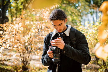 Fototapeta premium Young amateut photographer checking photos in his modern dslr camera, happy with results photographing autumn forest