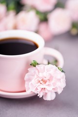 Pink cup of black coffee and pink carnation flower on a gray concrete background