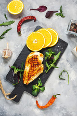 Grilled chicken fillets with orange on slate plate. Gray concrete background.