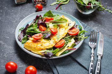 Herb omelette with cheese, cherry tomatoes and arugula on stone background. Breakfast