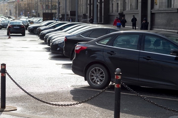 A row of cars parked in a Parking lot against the background of a street and pedestrians with a...