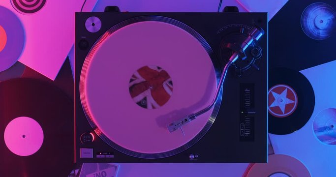 Turntable DJ player pink vinyl bright label in center on white surface with vinyls blue-red neon light lamps. Rotating plate close-up. Needle stylus. Loop. Top view. Popular Disco 60s, 70s, 80s, 90s