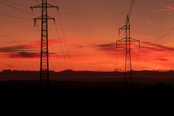 Silhouette of high voltage lines and transmission towers thru the Moravian field at sunrise