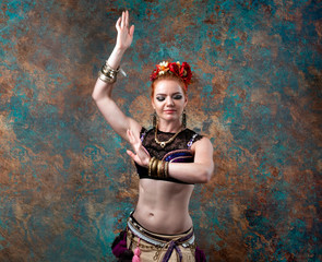 attractive woman in tradition tribal costume with vest, skirt and red floral circlet of flowers stay in pose in front of teal and orange background in studio