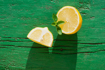 Yellow juicy lemon slices with mint leaves  on wooden green background with hard light, on strong sunlight with long dark shadow, contrast photography, mojito ingredients © Sunny_Smile