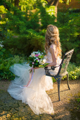 Young bride in a white wedding dress sits in a green garden