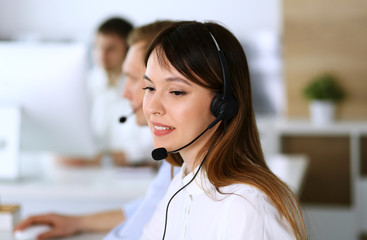 Call center. Group of diverse operators at work. Focus on beautiful asian woman in headset at customer service office. Business concept