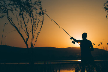Silhouette of a fisherman fishing on a lake at sunset