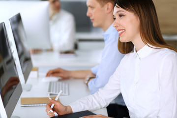 Obraz premium Cheerful smiling asian businesswoman headshot at work in modern office. Casual dressed female entrepreneur using pc computer while sitting with diverse colleagues at the background. Multi ethnic