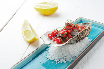 Fresh Oysters with tomato and herbs on the blue plate, table with oysters, lemon and salt. Table...