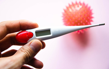 Influenza virus, coronavirus on a pink background near a thermometer. The thermometer in male hands. Temperature, disease, epidemic. COVID-19