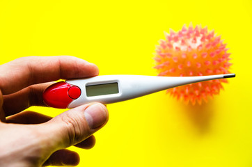 Influenza virus, coronavirus on a yellow background near a thermometer. The thermometer in male hands. Temperature, disease, epidemic. COVID-19