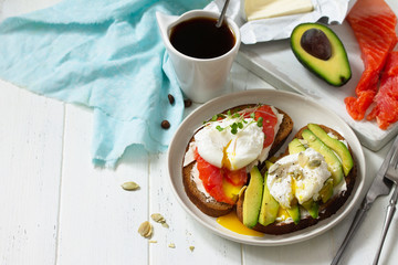 Morning breakfast. Poached egg boiled sandwich with avocado, salmon and coffee on a wooden table. Copy space.