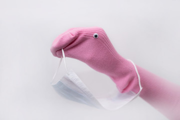 a baby pink sock is placed on the child's hand in the form of a duck and holds a medical mask