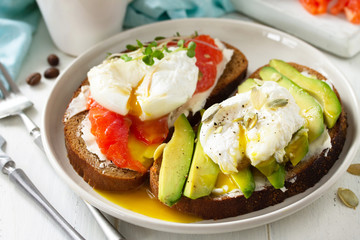 Morning breakfast close-up. Poached egg boiled sandwich with avocado, salmon and coffee on a wooden table.