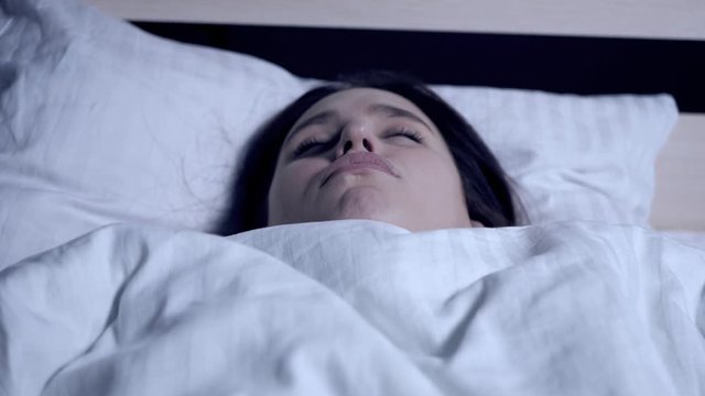 Girl snores. Stuffy nose, apnea, curvature of nasal septum, fatigue concept. Young attractive caucasian woman sleeps at night on her back in bed with open mouth. Close-up