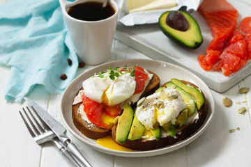 Morning breakfast. Poached egg boiled sandwich with avocado, salmon and coffee on a wooden table.