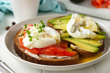 Morning breakfast close-up. Poached egg boiled sandwich with avocado, salmon and coffee on a wooden table.