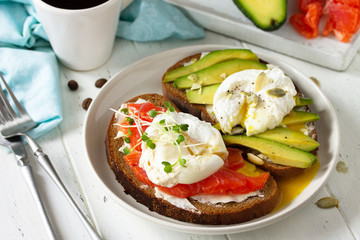 Morning breakfast. Poached egg boiled sandwich with avocado, salmon and coffee on a wooden table.