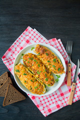Stuffed zucchini with minced meat and grated cheese in a white dish. Summer kitchen. Dark wooden background. Food background. Space for text.