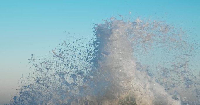 Splashes large strong waves on pier against background of bright blue sky on spring sunny day slow motion. Approaching wave with splashes of water. Strength and power of breaking wave on pier. Splash