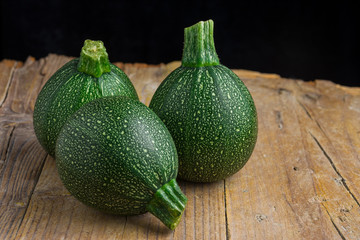 Top view of three round zucchini on rustic wooden board with selective focus and horizontal black...