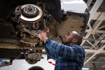 African male car mechanic repairing a car located on the car lift in the service center. Used car service