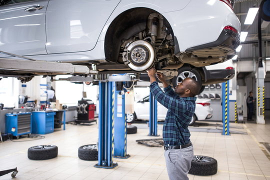 African male car mechanic repairing a car standing under the car located on the lift in the service center. Repair of brake discs