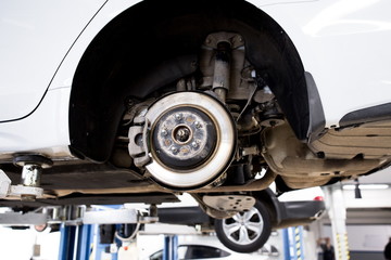 Car raised on the car lift. Brake disc with brake pads. A car with its wheels removed at a service station.