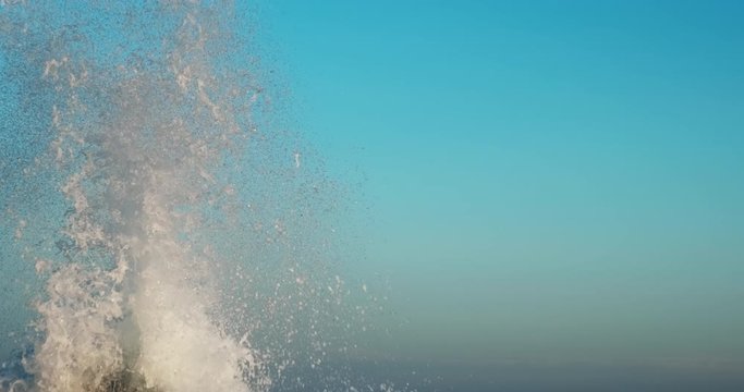 Splashes large strong waves on pier against background of bright blue sky on spring sunny day slow motion. Approaching wave with splashes of water. Strength and power of breaking wave on pier. Splash
