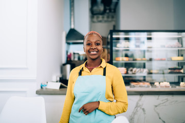 Happy ethnic adult self employed woman against blurred counter and showcase in own cafe
