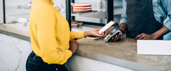 Joyful cafe owner waiting while customer making mobile payment