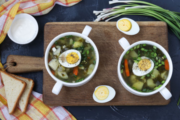 Green borsch with sorrel and egg in two white bowls on wooden board on a dark background