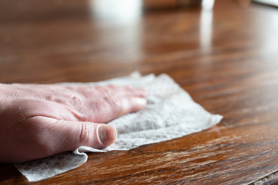 Hand holding sanitizing wipe to disinfect a wooden table top