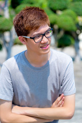 Hight angle shot Asian handsome teenage boy wearing glasses standing arms crossed, Portrait cheerful hipster young man smile with a happy face at park in Thailand