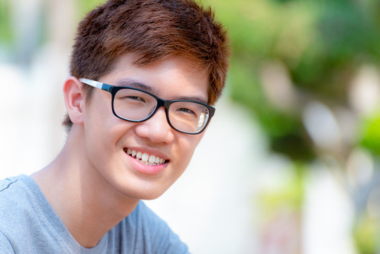 Closeup face Asian handsome teenage boy wearing glasses, Portrait cheerful hipster young man are smiling with a happy face at park on green nature background in Thailand