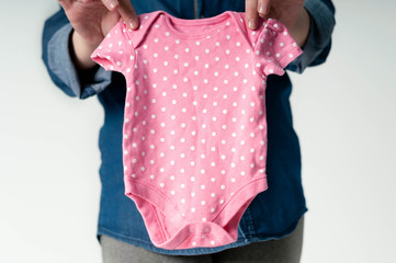 selective focus of pregnant woman in blue jeans shirt holding pink polka dot bodysuit on white background