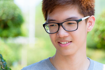Closeup face Asian handsome teenage boy wearing glasses, Portrait cheerful hipster young man smile with a happy at park on green nature background in Thailand