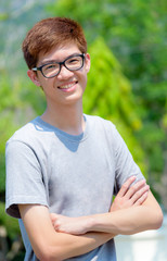 Asian handsome teenage boy wearing glasses standing arms crossed, Portrait cheerful hipster young man are looking and smile with a happy face at park in Thailand