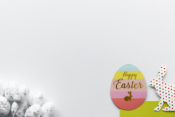 Colorful easter egg card with Happy Easter wishes and paper easter bunny on green grass. White eggs with silver details. Copy space on white background.