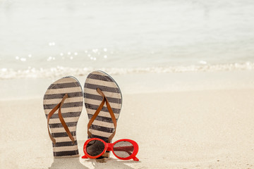 Sunglasses and flip flops on a tropical sand beach. Travel, vacation concept.