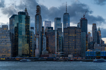 New York City Manhattan Skyline at dusk with lights on and clouds from Brooklyn bridge park over the river Hudson after Sunset. Freedom Tower Financial District one world trade center night life  