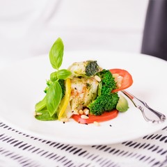 Steamed cod fish fillet with broccoli, tomato, lemon, avocado, basil sauce and pine nuts on a white background. Copy space