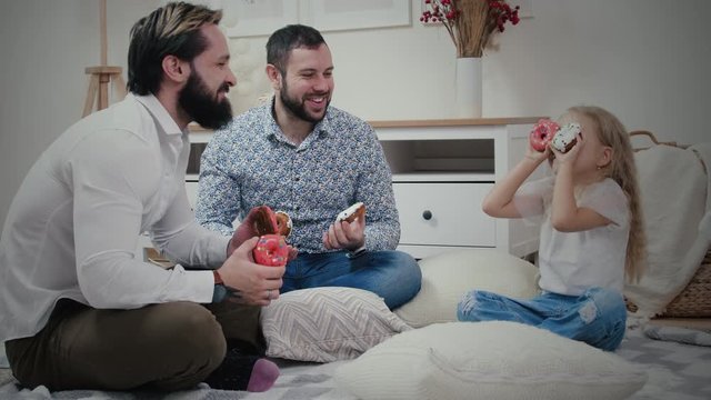 Little girl with her dads having fun with donuts
