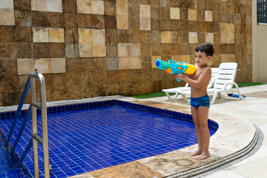 6 Year Old Child Standing And Firing His Squirt Gun At His Doll.