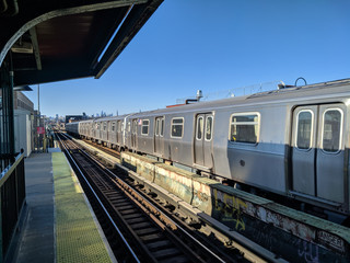 Train at platform in long Island, New York, Queens, with the skyline in the background in a sunny...