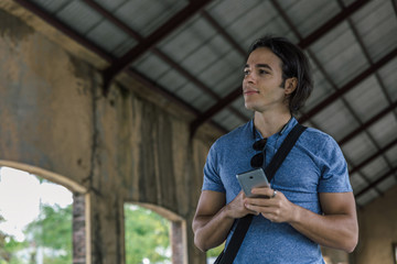 Attractive young man in a blue T-shirt, hanging black glasses and a smartphone in his hands looks thoughtfully