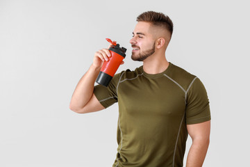 Sporty man with protein shake on light background